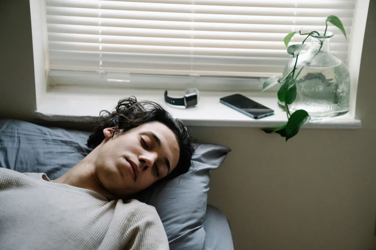 Young man sleeping in bed with a smartwatch and smartphone nearby.